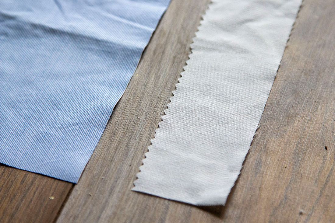 A close up of the blue fabric top with the pinked edge of the muslin interfacing sitting to the right of it on a dark wooden floor. 